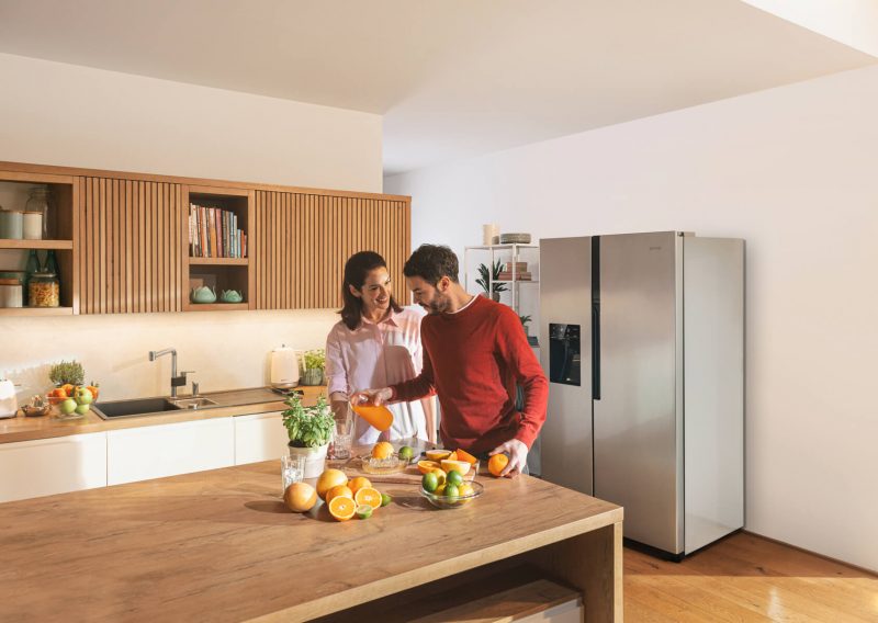 Жінка й чоловік готують їжу на кухні в спокійних відтінках перед холодильником Gorenje.